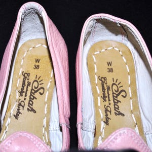 May include: A pair of pink leather ballet flats with a white leather lining. The inside of the shoes has a label that reads "Sıbaf Handmade in Turkey" and "W 38".