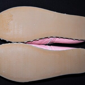 May include: The bottom of a pair of pink leather shoes with white stitching. The soles are brown and textured.
