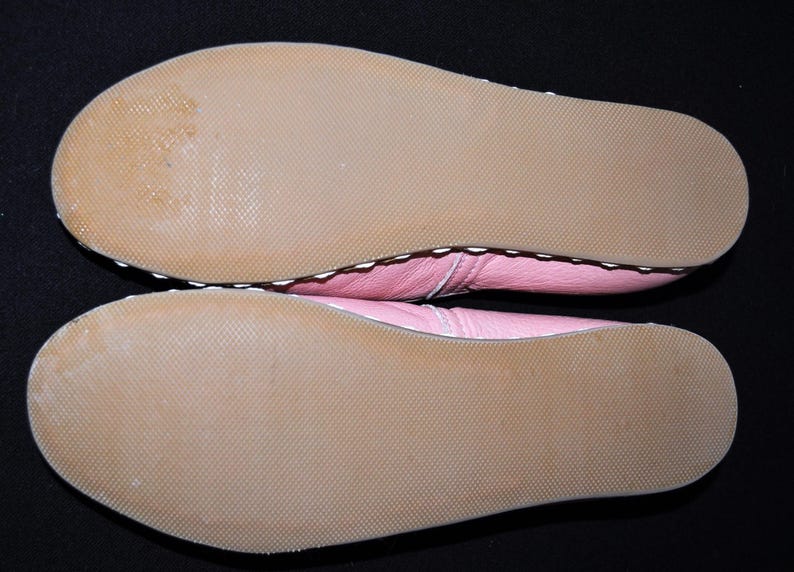 May include: The bottom of a pair of pink leather shoes with white stitching. The soles are brown and textured.
