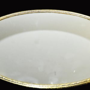 May include: A gold oval tray with a mirrored surface and ornate floral designs on the handles.