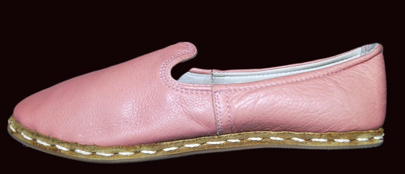 May include: A pair of pink leather slip-on shoes with a white stitched trim around the sole.