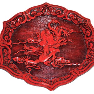 Peut inclure: Plaque décorative ovale rouge avec un motif en relief sculpté. L'image centrale représente une figure avec des dragons et des nuages. La bordure est finement sculptée avec un motif répétitif. La plaque est peinte en rouge brillant.