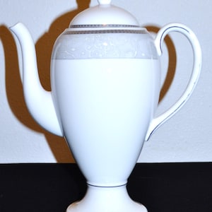 Puede incluir: Cafetera de porcelana blanca con un diseño floral plateado y gris y un pomo dorado en la tapa.