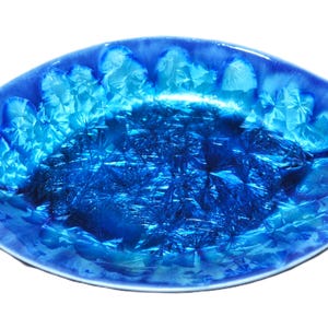 May include: A decorative, oval-shaped ceramic bowl with a striking blue crystalline pattern. The bowl's interior features a deep, textured blue, while the rim transitions to a lighter shade. This unique piece is ideal for serving or display.