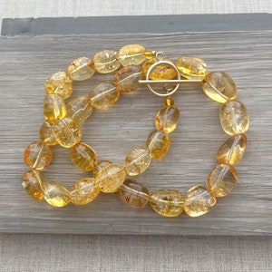 May include: A gold necklace with a toggle clasp made of oval-shaped, translucent, yellow citrine beads.