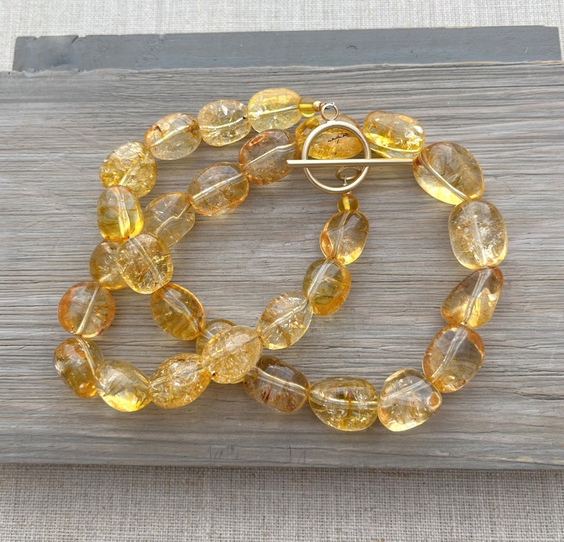 May include: A gold necklace with a toggle clasp made of oval-shaped, translucent, yellow citrine beads.
