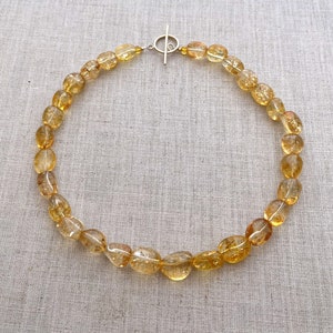 May include: A gold necklace made of oval-shaped, translucent, yellow citrine beads. The necklace has a silver toggle clasp.