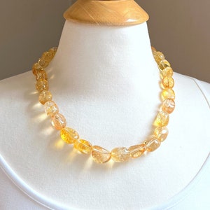 May include: A necklace made of golden citrine gemstone beads. The beads are faceted and have a translucent, slightly cloudy appearance. The necklace is strung on a thin, silver chain.