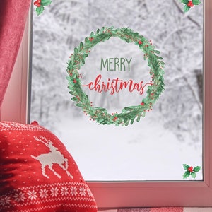 Op de afbeelding: Een raam met een rood gordijn en een rood-wit gestreept kussen. Op het raam zit een groene krans met rode bessen en de tekst "Merry Christmas".