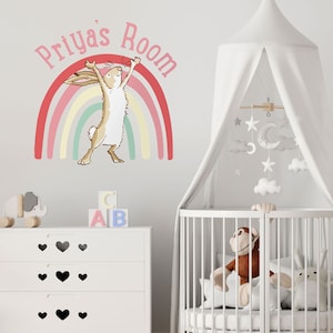 May include: A white crib with a white canopy and a mobile hanging above it. The mobile has white clouds, stars, and a crescent moon. There is a stuffed animal monkey sitting in the crib. The wall behind the crib has a pink and rainbow wall decal with a rabbit jumping over the rainbow. The text "Priya's Room" is written above the rainbow.