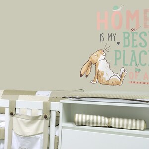 May include: A wall decal featuring a whimsical illustration of a rabbit with the text "HOME IS MY BEST PLACE OF ALL." The design includes a snail, ladybug, and other decorative elements. The decal is in soft pastel colors.