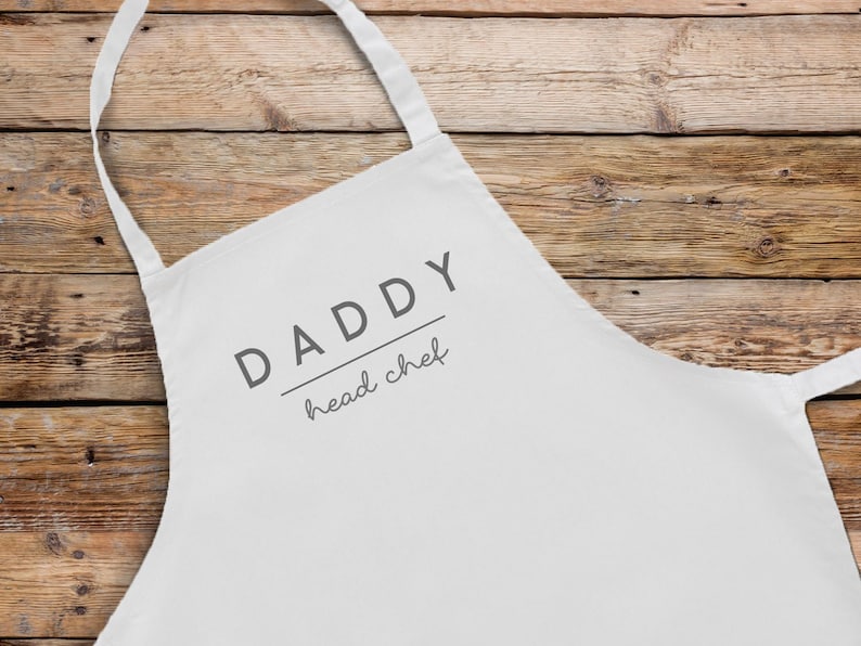 May include: White apron with the text "DADDY head chef" printed on it.