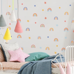 Op de afbeelding: Een wit metalen bedframe met een roze en wit gestreept dekbed en een roze stervormig kussen. De muur achter het bed is versierd met regenboog- en ster stickers.