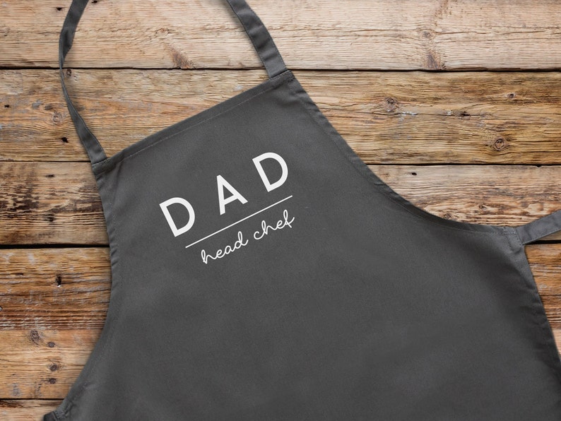 May include: Grey apron with white text that reads "DAD head chef".