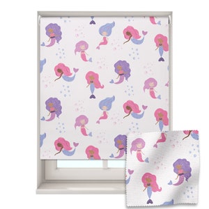 May include: A white roller blind with a repeating pattern of mermaids with purple and pink hair and tails. The mermaids are swimming in a sea of white bubbles. The blind is shown partially rolled up, revealing a white fabric with a similar pattern.