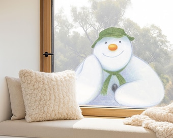 May include: A cozy window seat features two cream-colored pillows and a soft, textured blanket. A whimsical illustration of a snowman with a green hat and scarf is visible through the window, creating a warm and inviting scene.