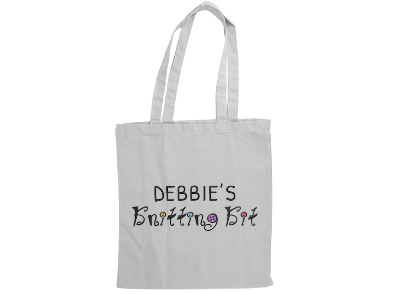 May include: White canvas tote bag with black text that reads "Debbie's Knitting Bit" with colorful buttons around the text.