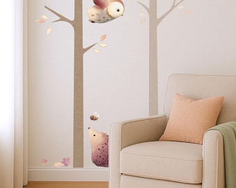 May include: A whimsical wall decal set featuring a forest scene with an owl, bird, hedgehog, and bee. The design includes brown tree trunks, leaves, and flowers in soft pastel colors. A beige armchair with a peach pillow and green blanket is in the corner.