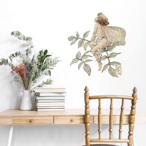 May include: A watercolor illustration of a fairy sitting on a branch with green leaves and white flowers. The fairy has long blonde hair and is wearing a white dress with a pink sash. The illustration is on a white background.