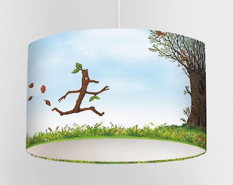 May include: A cylindrical lampshade featuring a whimsical illustration. The design depicts a stick figure with leaves for hair and arms, running across a grassy field. A large tree and blue sky complete the scene. The lampshade is suspended from a white cord.