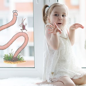 May include: A young girl in a white lace dress sits by a window with a cartoon worm and bug sticker on the glass. The girl is looking at the camera with a surprised expression.