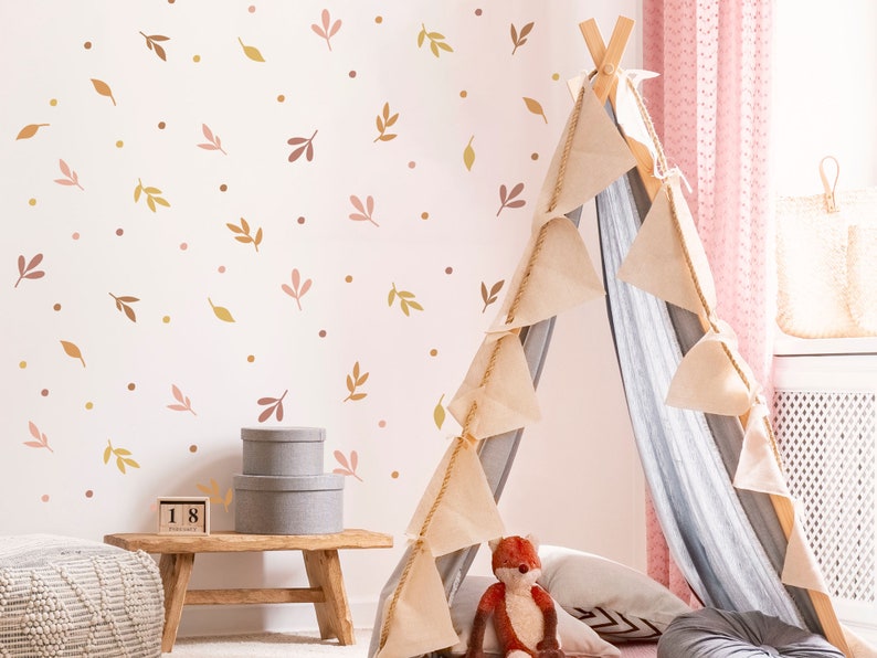 May include: A white wall with pink and brown leaf and dot decals. A teepee tent with a gray and white striped fabric interior is in the corner of the room. The teepee has a brown wooden frame and beige fabric flaps. A stuffed fox is sitting inside the teepee.