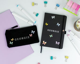 May include: A black zippered pencil case with the name "Georgie" and colourful butterfly designs. A black notebook with the same name and butterfly designs is also pictured.