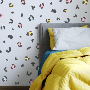 Könnte beinhalten: Ein Bett mit einer gelben Bettdecke und einem grauen Kopfteil. Die Wand hinter dem Bett ist mit schwarzen, rosa, blauen und gelben Leoparden-Aufklebern verziert.
