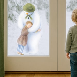 Op de afbeelding: Een hartverwarmende illustratie toont een sneeuwman die een kind omhelst. De sneeuwman draagt een groene hoed en sjaal, het kind een bruin outfit en blauw gestreepte broek. Een jong kind staat in de buurt en bekijkt de scène.