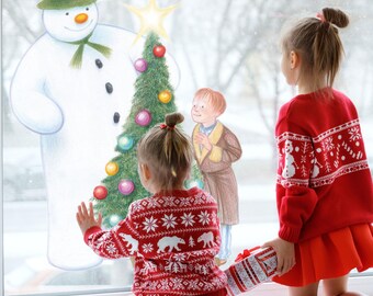 May include: Two young children in red sweaters with white snowflake and bear patterns look at a Christmas scene on a window. The scene includes a snowman, a decorated Christmas tree, and a boy in a coat. One child holds a wrapped gift.