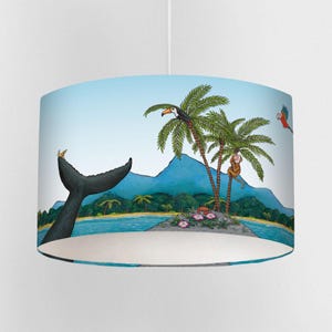 May include: A lampshade with a tropical island illustration. The design features a whale's tail, palm trees with a toucan and monkey, and a parrot. The background shows a light blue sky and ocean with a small island.