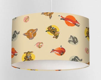 May include: A cylindrical lampshade featuring a repeating pattern of whimsical forest animals, including foxes, owls, and snakes, set against a light beige background. The illustrations are in a cartoon style, with each animal inside a yellow or pink circle.