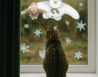 May include: A tabby cat sits on a windowsill, gazing out at a whimsical scene. A snowman with a green hat and scarf floats near a boy in a brown coat, surrounded by snowflakes. The image has a storybook illustration style.