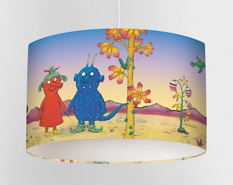May include: A cylindrical lampshade featuring a whimsical illustration of two cartoon monsters holding hands in a desert landscape. The design includes a blue sky, a yellow tree, and a variety of colorful plants and creatures.