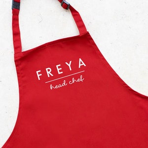 May include: Red apron with white text that says "FREYA head chef".