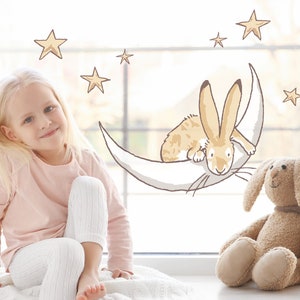 May include: A young girl sits on a white blanket in front of a window with a whimsical illustration of a bunny on a crescent moon and stars.