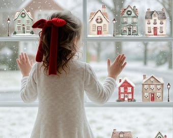 May include: A young person with a red bow in their hair looks out a window at a snowy scene. Decorative miniature houses and street lamps are affixed to the window, creating a winter village scene. The houses are various colors and styles.