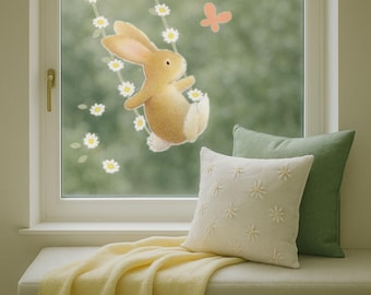 May include: A window scene featuring a cartoon bunny on a daisy swing, with a butterfly and bee. A white bench holds a yellow blanket, a white pillow with daisy accents, and a green pillow. The window is framed in white.