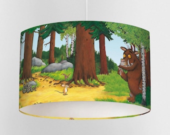 May include: A cylindrical lampshade featuring a forest scene with cartoon characters. The design includes tall trees, a path, and a brown monster with a mouse. The color palette includes green, brown, yellow, and blue.