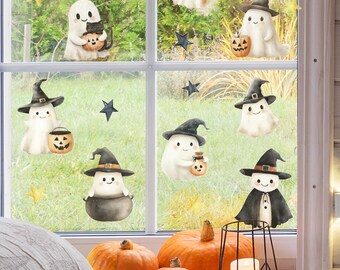 May include: A window decorated with Halloween-themed stickers featuring cartoon ghosts wearing witch hats and holding jack-o'-lanterns. Orange pumpkins and a candle holder are in front of the window, creating a festive autumn scene.
