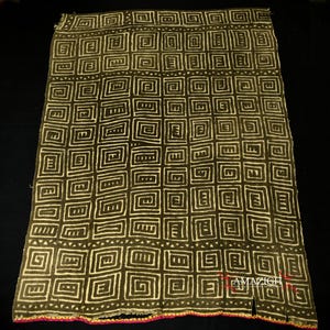 Puede incluir: Textil verde oscuro con un patrón repetitivo de cuadrados blancos y formas geométricas. La tela tiene un borde decorativo con hilos rosas y amarillos. La palabra "AMAZIGH" es visible en la esquina inferior derecha.