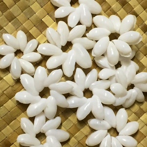 May include: A collection of white shell flower-shaped ornaments, arranged on a woven straw mat.