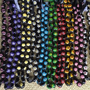 May include: A collection of colorful Hawaiian leis made with black wooden beads painted with floral designs. The leis are arranged in a row, with each lei featuring a different color flower.