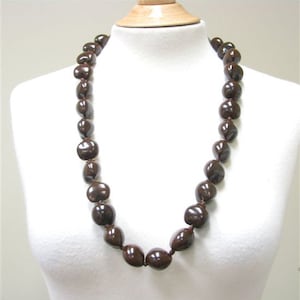 May include: A brown seed lei necklace made of natural materials. The necklace is strung on a brown cord and is approximately 30 inches long.
