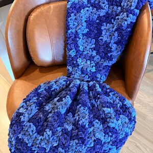 May include: A chunky crochet blanket featuring a variegated pattern of deep navy, royal blue, and light sky blue yarn. The textile has a thick, soft, and textured appearance with a consistent looped stitch throughout the entire piece.