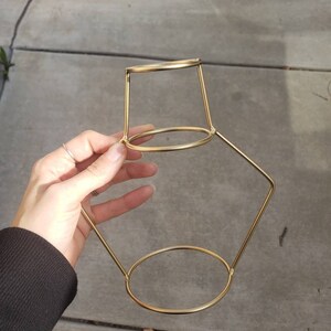 May include: Gold metal plant stand with a round top and two tiers. The stand is made of thin metal and has a geometric shape.