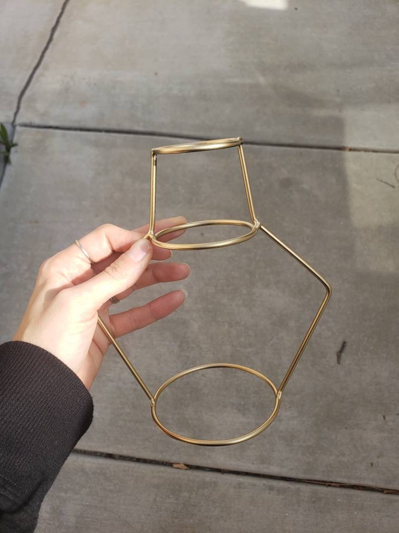 May include: Gold metal plant stand with a round top and two tiers. The stand is made of thin metal and has a geometric shape.