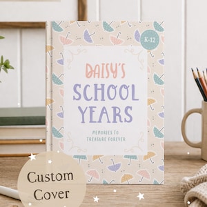 Może przedstawiać: Spersonalizowana książka wspomnień szkolnych zatytułowana "Daisy's School Years" z jasnobeżową okładką ozdobioną pastelowymi parasolami. Książka zawiera tekst "Memories to Treasure Forever" i naklejkę "K-12".