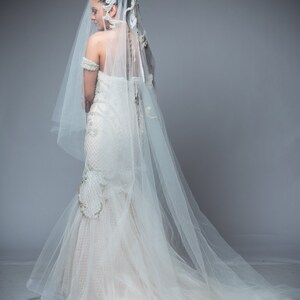 Puede incluir: Una novia con un vestido de novia blanco con un velo largo y un tocado decorativo. El vestido tiene un corpi&ntilde;o ajustado y una falda fluida.