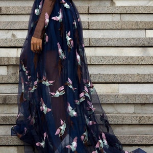May include: A long, navy blue tulle gown with a sheer bodice and embroidered floral designs. The gown has a fitted bodice and a flowing skirt.